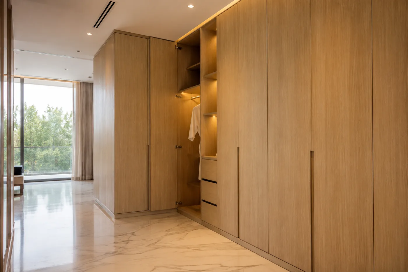 Floor-to-ceiling timber wardrobe doors beside an open hanging section, in a bedroom with a glazed wall